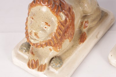 Lot 28 - A PAIR OF 19TH CENTURY GLAZED PAINTED STONEWARE RECUMBENT LIONS